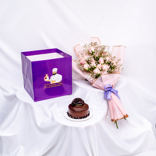 An elegant gift set including a rich chocolate bento cake, a soft pink rose bouquet with baby's breath, and a signature 'Let's Bake Cake' purple gift bag on a white silk backdrop, Abu Dhabi.