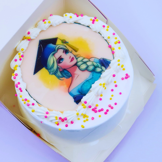 A white graduation cake with an Elsa Frozen edible image, white frosting swirls, and pink/gold sprinkles by Let's Bake Cake Abu Dhabi.