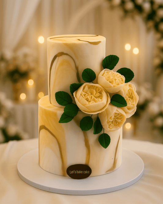 A luxury two-tier wedding cake with a cream and gold marble finish and ivory sugar flowers by Let's Bake Cake Abu Dhabi.