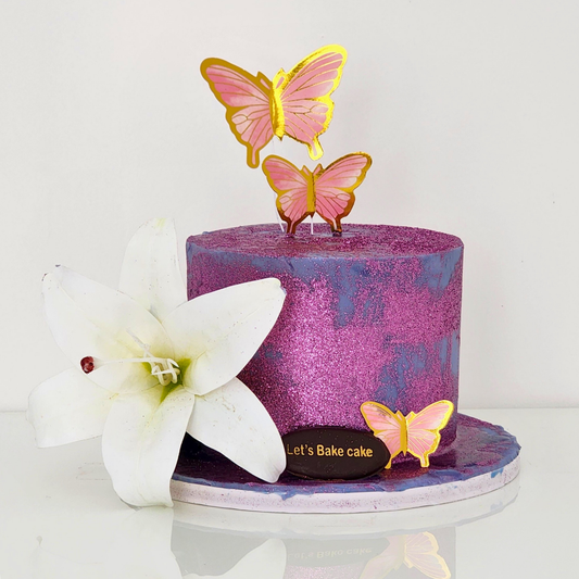 A luxury purple glitter-textured birthday cake decorated with pink butterflies and a large white lily by Let's Bake Cake Abu Dhabi