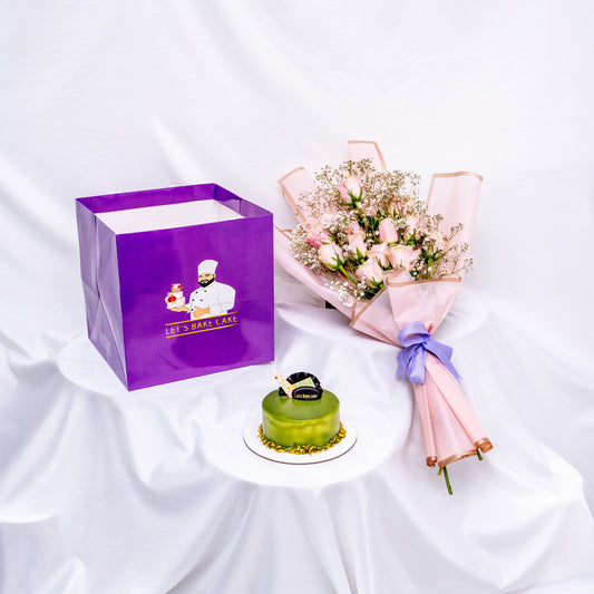 A luxury gift set featuring a green pistachio glazed bento cake, a delicate pink rose bouquet, and a signature 'Let's Bake Cake' purple gift bag on white silk, Abu Dhabi.
