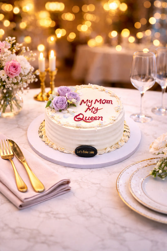 A luxury white celebration cake with 'My Mom My Queen' written in red, decorated with lavender roses, set on a marble table with gold cutlery and warm bokeh lighting, by Let's Bake Cake Abu Dhabi.