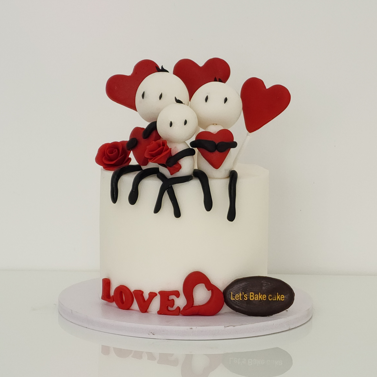 A custom white anniversary cake decorated with handcrafted fondant family figures, red hearts, and 'LOVE' lettering by Let's Bake Cake Abu Dhabi