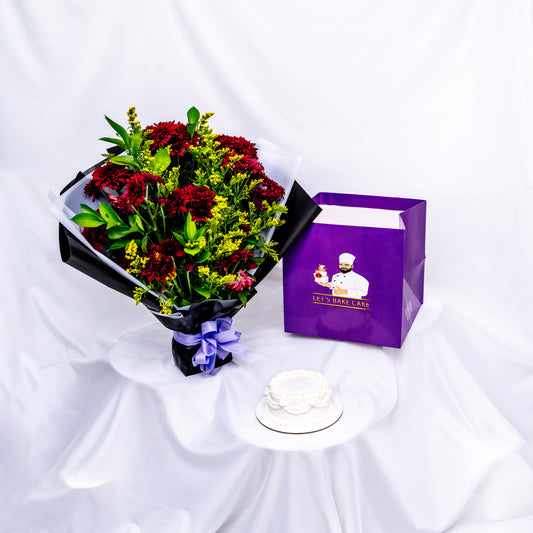 An elegant gift set featuring a hand-piped white bento cake, a vibrant red and yellow flower bouquet in black wrap, and a signature 'Let's Bake Cake' purple gift bag on white silk, Abu Dhabi.