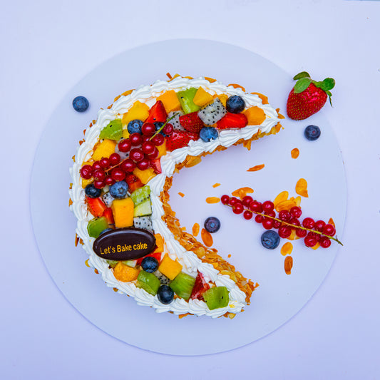 A luxury crescent moon-shaped cake topped with fresh dragon fruit, kiwi, mango, and berries, decorated with roasted almonds and cream by Let's Bake Cake Abu Dhabi.