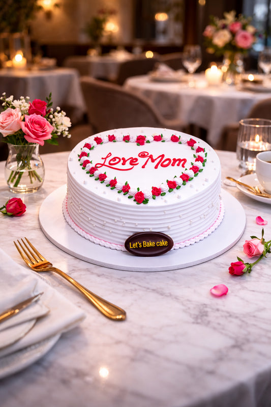 A luxury white celebration cake with 'Love Mom' written in red, decorated with a heart-shaped border of red rose-buds, set on a marble table with gold cutlery in a premium Abu Dhabi restaurant, by Let's Bake Cake.