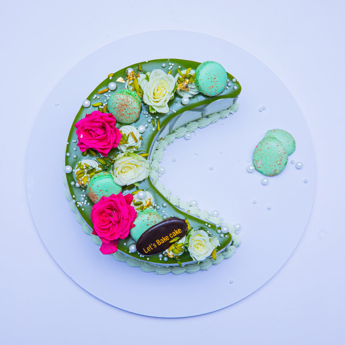 A luxury chocolate mirror-glazed crescent moon cake decorated with Ferrero Rocher, fresh strawberries, chocolate macaroons, and gold leaf by Let's Bake Cake Abu Dhabi.