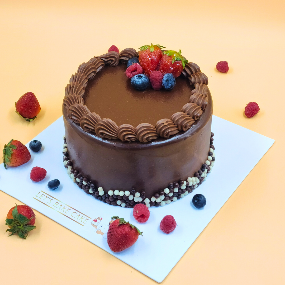 A luxury dark chocolate ganache cake with fresh strawberries, blueberries, and chocolate crisp pearls by Let's Bake Cake Abu Dhabi.