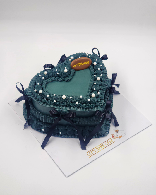 A luxury dark teal heart-shaped vintage piped cake with navy blue satin bows and white pearls by Let's Bake Cake Abu Dhabi.