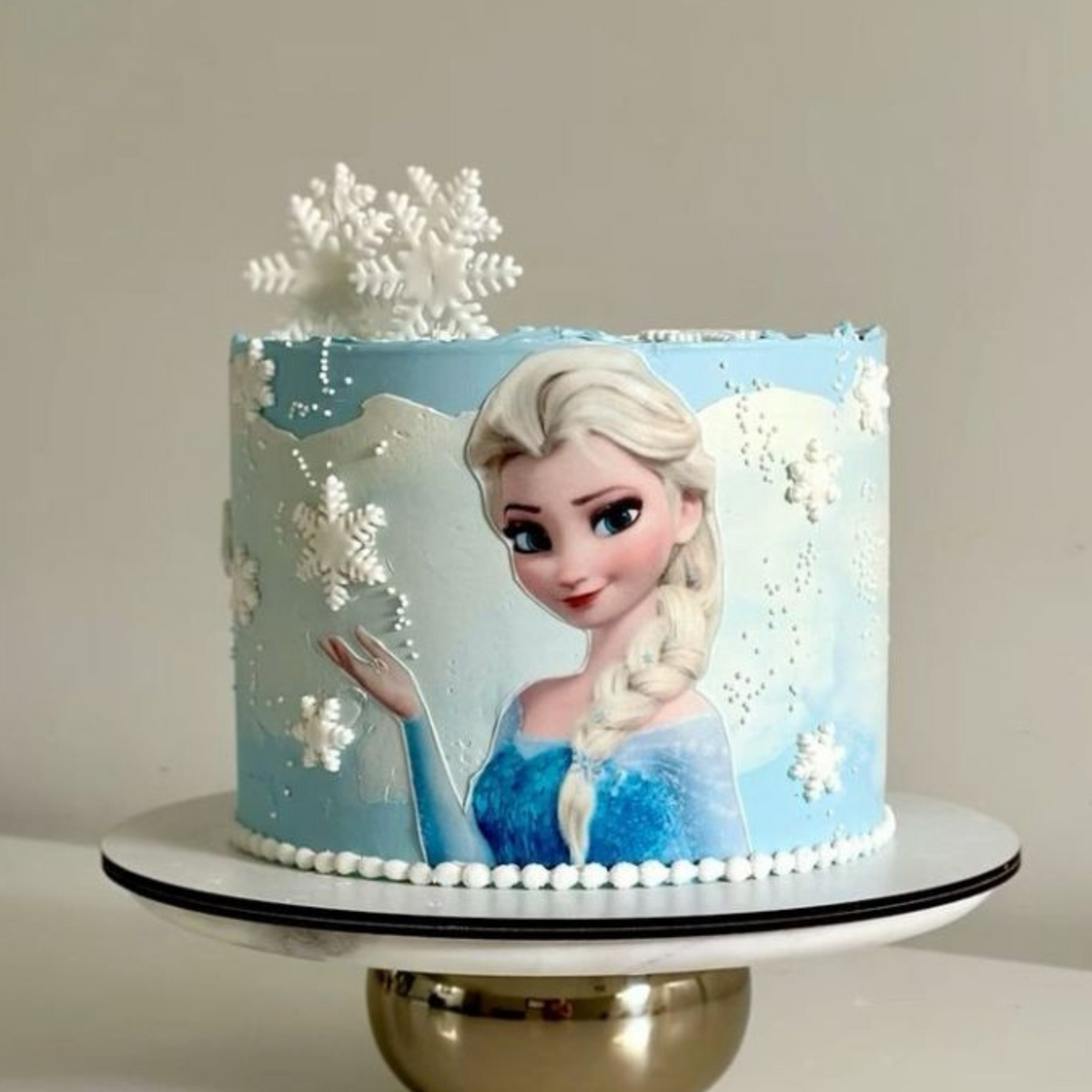 A luxury Elsa Frozen-themed birthday cake with 3D snowflakes and white pearl detailing by Let's Bake Cake Abu Dhabi.