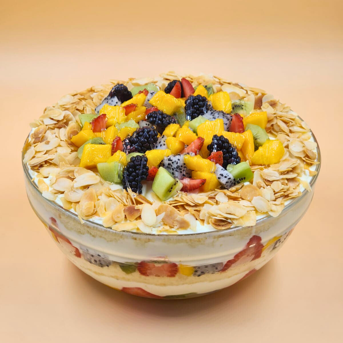 A luxury glass bowl filled with layered fruit trifle, topped with fresh dragon fruit, mango, berries, and toasted almond flakes by Let's Bake Cake Abu Dhabi.