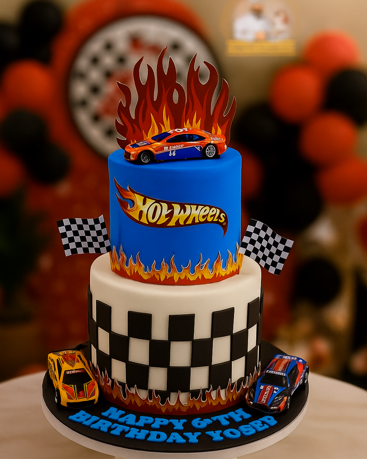 A luxury two-tier Hot Wheels themed birthday cake with racing cars, flames, and checkered flag patterns by Let's Bake Cake Abu Dhabi