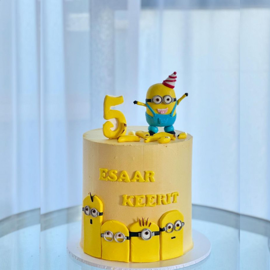 A luxury yellow Minions-themed birthday cake with a 3D Minion topper and personalized names by Let's Bake Cake Abu Dhabi