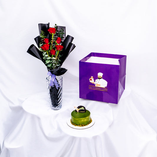 A luxury gift combo featuring a green pistachio glazed bento cake, a premium glass vase with long-stemmed red roses, and a signature 'Let's Bake Cake' purple gift bag, Abu Dhabi.