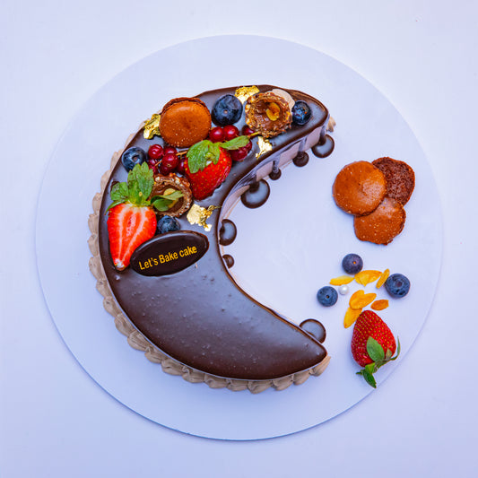 A luxury crescent moon cake with green pistachio mirror glaze, decorated with pink roses, mint macaroons, and gold leaf by Let's Bake Cake Abu Dhabi.