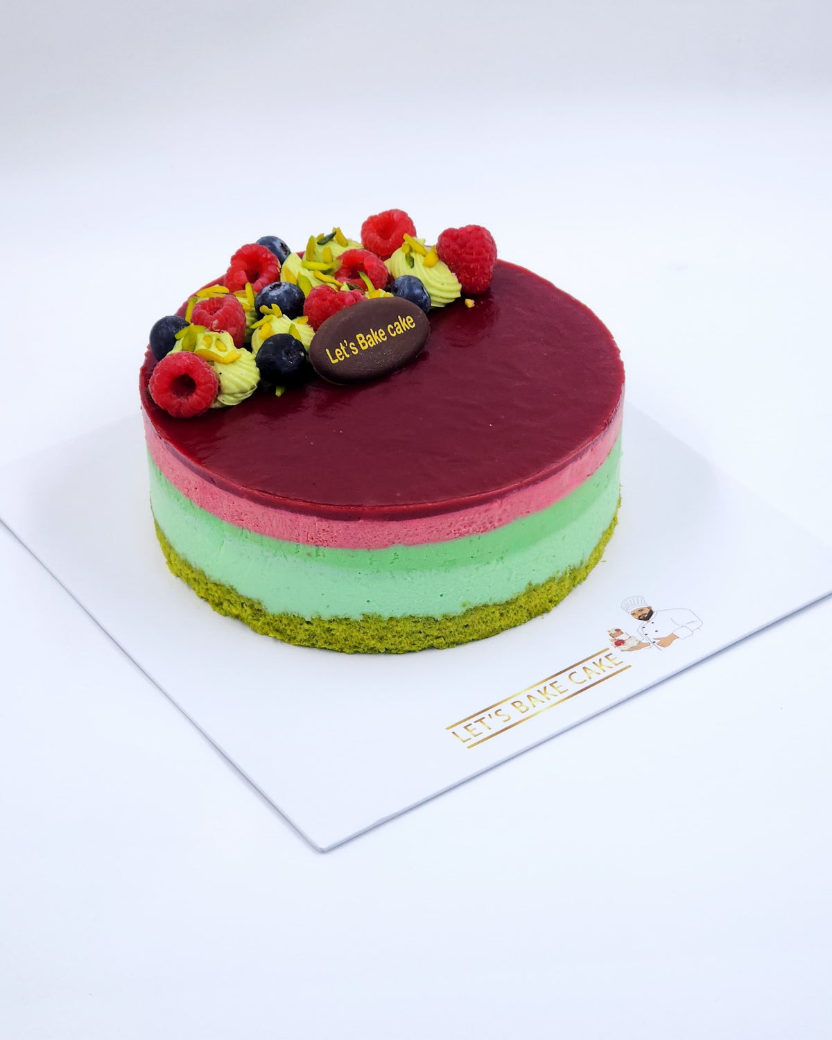 A luxury pistachio and berry layered mousse cake with green and pink layers, topped with fresh raspberries and blueberries by Let's Bake Cake Abu Dhabi.