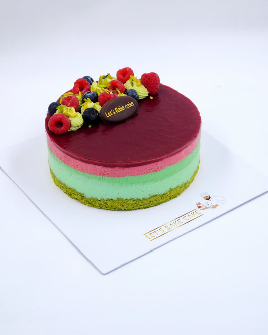 A luxury pistachio and berry layered mousse cake with green and pink layers, topped with fresh raspberries and blueberries by Let's Bake Cake Abu Dhabi.