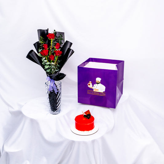 A luxury gift combo featuring a vibrant red mirror-glazed bento cake, a premium glass vase with red roses and eucalyptus, and a signature 'Let's Bake Cake' purple gift bag, Abu Dhabi.