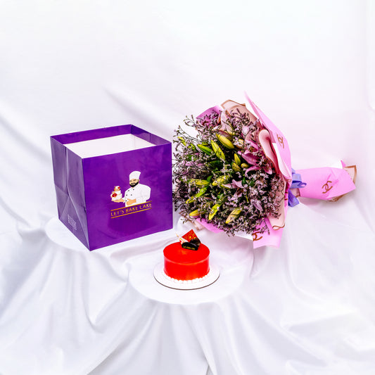 A luxury gift set featuring a vibrant red mirror-glazed bento cake, a large pink lily bouquet in designer wrap, and a signature 'Let's Bake Cake' purple gift bag on white silk, Abu Dhabi.