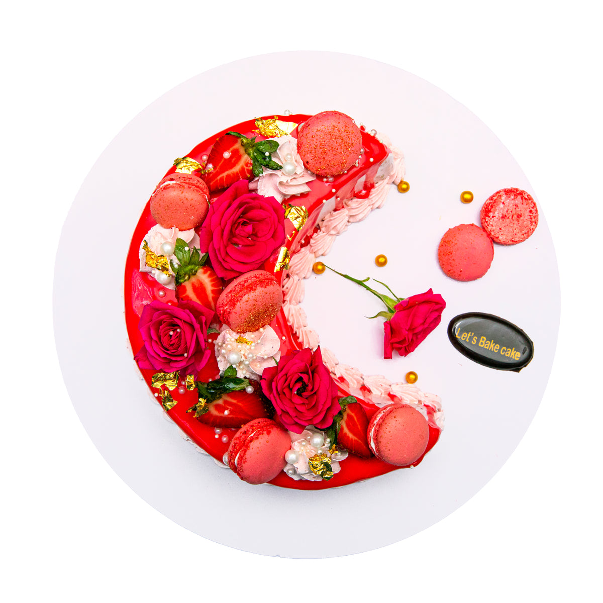 A luxury red mirror-glazed crescent moon cake decorated with fresh red roses, strawberry macaroons, and edible gold leaf by Let's Bake Cake Abu Dhabi.