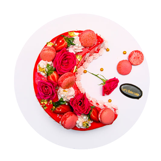 A luxury red mirror-glazed crescent moon cake decorated with fresh red roses, strawberry macaroons, and edible gold leaf by Let's Bake Cake Abu Dhabi.
