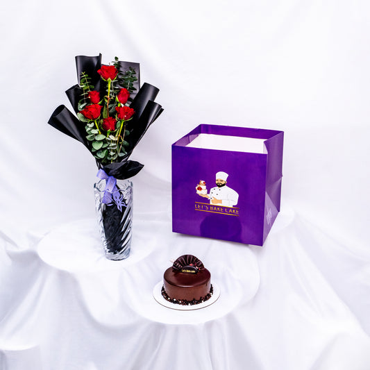 A luxury gift combo featuring long-stemmed red roses in a glass vase, a rich chocolate glazed bento cake, and a signature 'Let's Bake Cake' purple gift bag, Abu Dhabi.