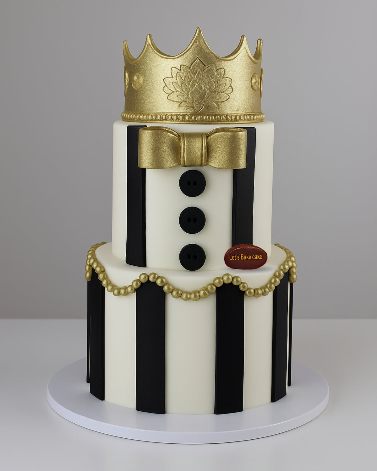 A luxury two-tiered black and white striped birthday cake topped with a majestic gold crown and gold pearl decorations by Let's Bake Cake Abu Dhabi.