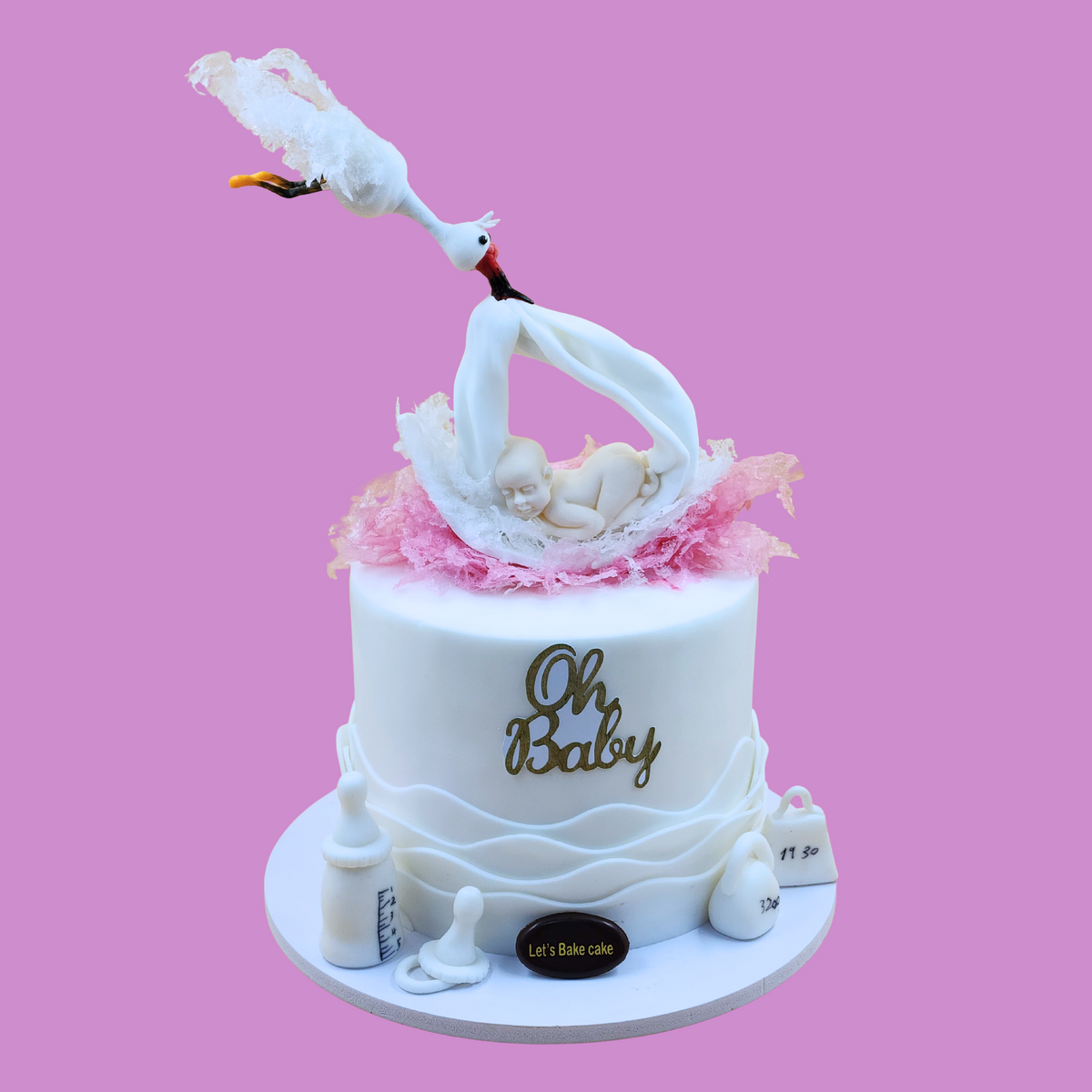 A luxury white baby shower cake featuring a handcrafted stork carrying a baby, with edible baby accessories and a gold 'Oh Baby' topper by Let's Bake Cake Abu Dhabi.