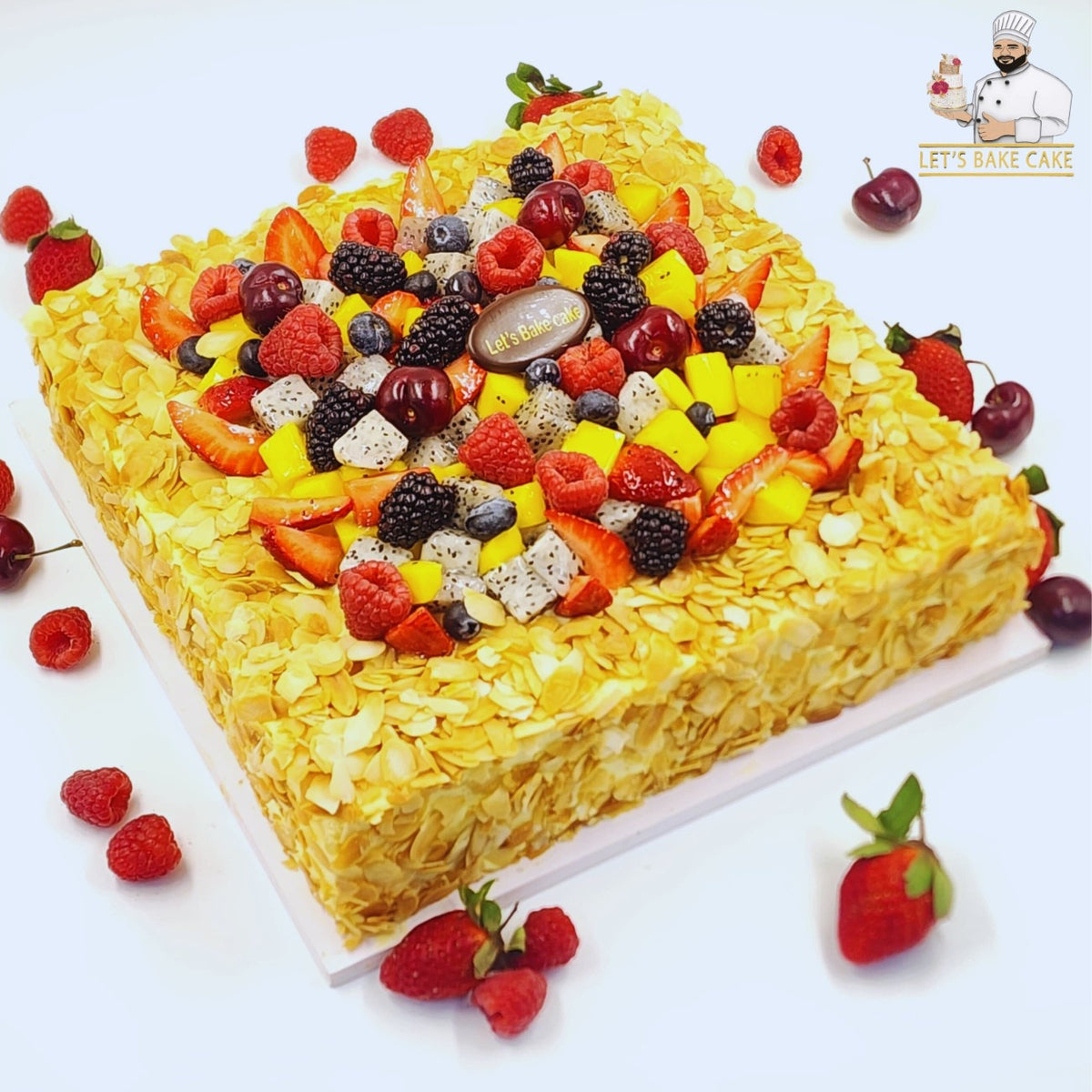A luxury square cake coated in toasted almond flakes and topped with a vibrant mix of dragon fruit, mango, cherries, and berries by Let's Bake Cake Abu Dhabi