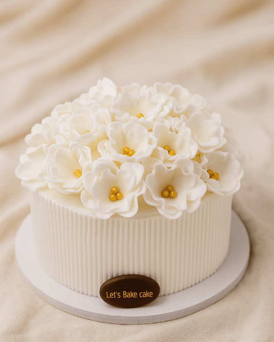 A luxury white cake with vertical stripe texture and handcrafted ivory flowers with gold centers by Let's Bake Cake Abu Dhabi.