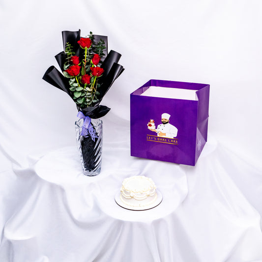 A luxury gift combo featuring a hand-piped white bento cake, a premium glass vase with long-stemmed red roses, and a signature 'Let's Bake Cake' purple gift bag, Abu Dhabi.