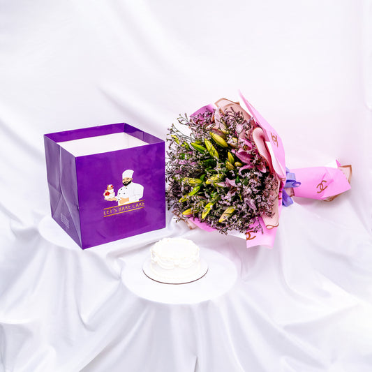 A luxury gift set featuring a hand-piped white bento cake, a large pink lily bouquet in designer wrap, and a signature 'Let's Bake Cake' purple gift bag on white silk, Abu Dhabi.