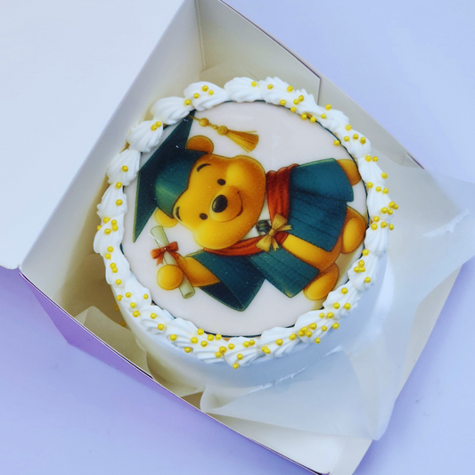 A white graduation cake featuring an edible image of Winnie the Pooh in a graduation cap and gown by Let's Bake Cake Abu Dhabi.