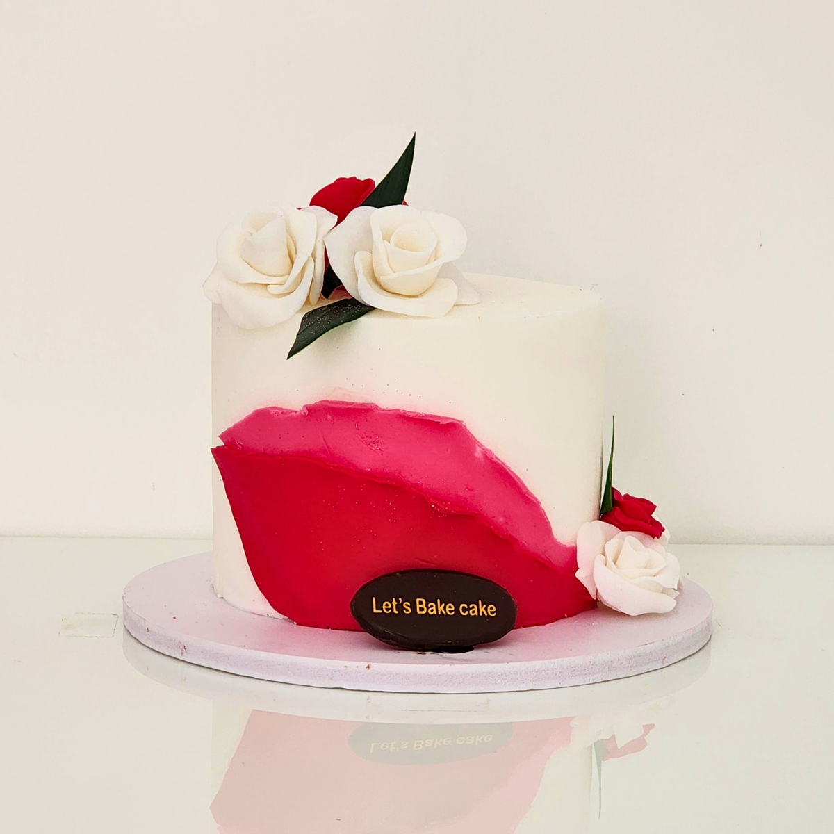 A modern white minimalist cake featuring a bold red buttercream stroke and decorated with white and red roses by Let's Bake Cake Abu Dhabi.