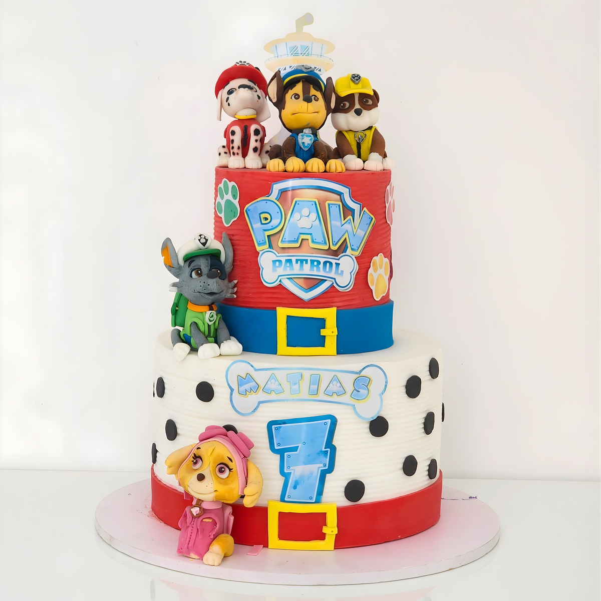 A premium two-tier Paw Patrol themed birthday cake with 3D fondant characters, dalmatian spots, and a lookout tower for a 7th birthday by Let's Bake Cake Abu Dhabi.