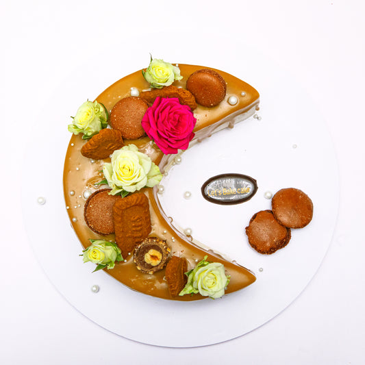 A luxury Lotus Biscoff mirror-glazed crescent moon cake decorated with fresh roses, Biscoff biscuits, macaroons, and Ferrero Rocher by Let's Bake Cake Abu Dhabi.