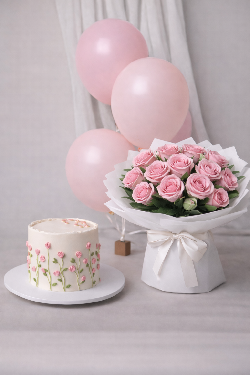 A luxury pastel pink gift bundle featuring a white cake with pink floral piping, a large bouquet of fresh pink roses, and pink balloons by Let's Bake Cake Abu Dhabi