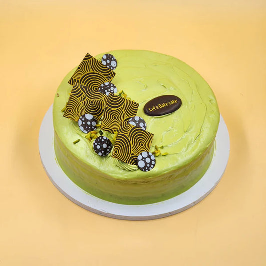 A premium Pistachio cake with smooth light green frosting, topped with artistic chocolate shards and crushed pistachios, handcrafted by Let's Bake Cake in Abu Dhabi