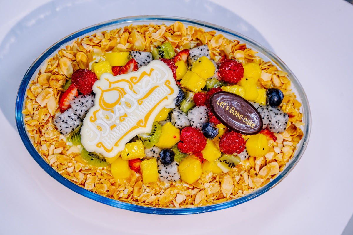 A premium Ramadan fruit trifle topped with kiwi, mango, dragon fruit, and berries, surrounded by a layer of roasted almonds in a glass dish by Let's Bake Cake, Abu Dhabi.