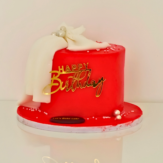 A modern red birthday cake decorated with a white fondant drape, silver pearls, and a gold acrylic 'Happy Birthday' topper by Let's Bake Cake Abu Dhabi.
