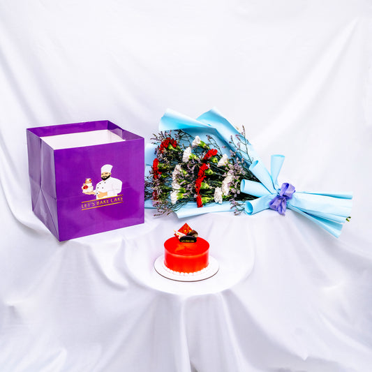 A premium gift set featuring a vibrant red mirror-glazed bento cake, a fresh red and white flower bouquet in sky-blue wrap, and a signature 'Let's Bake Cake' purple gift bag on white silk, Abu Dhabi.